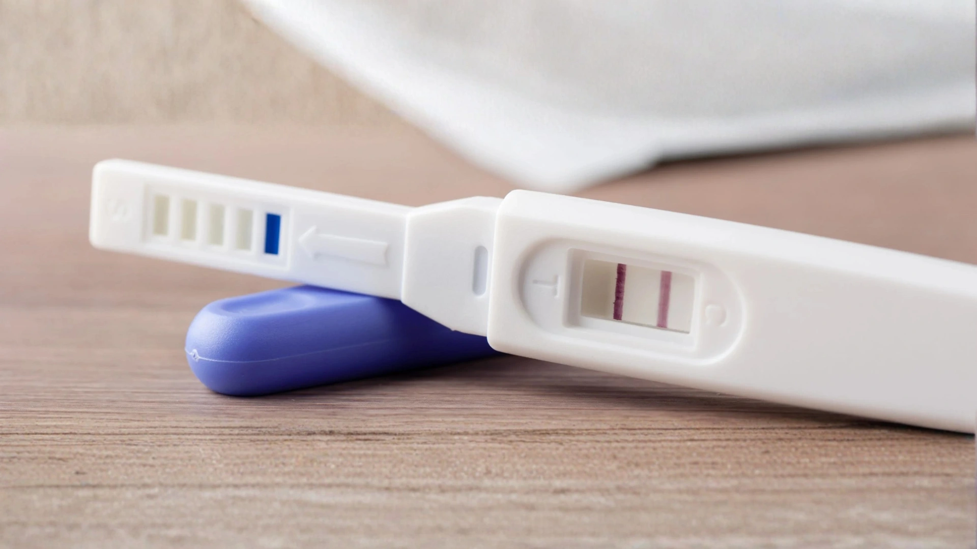 A pregnancy test with two pink lines indicating a positive result is placed on a wooden table.