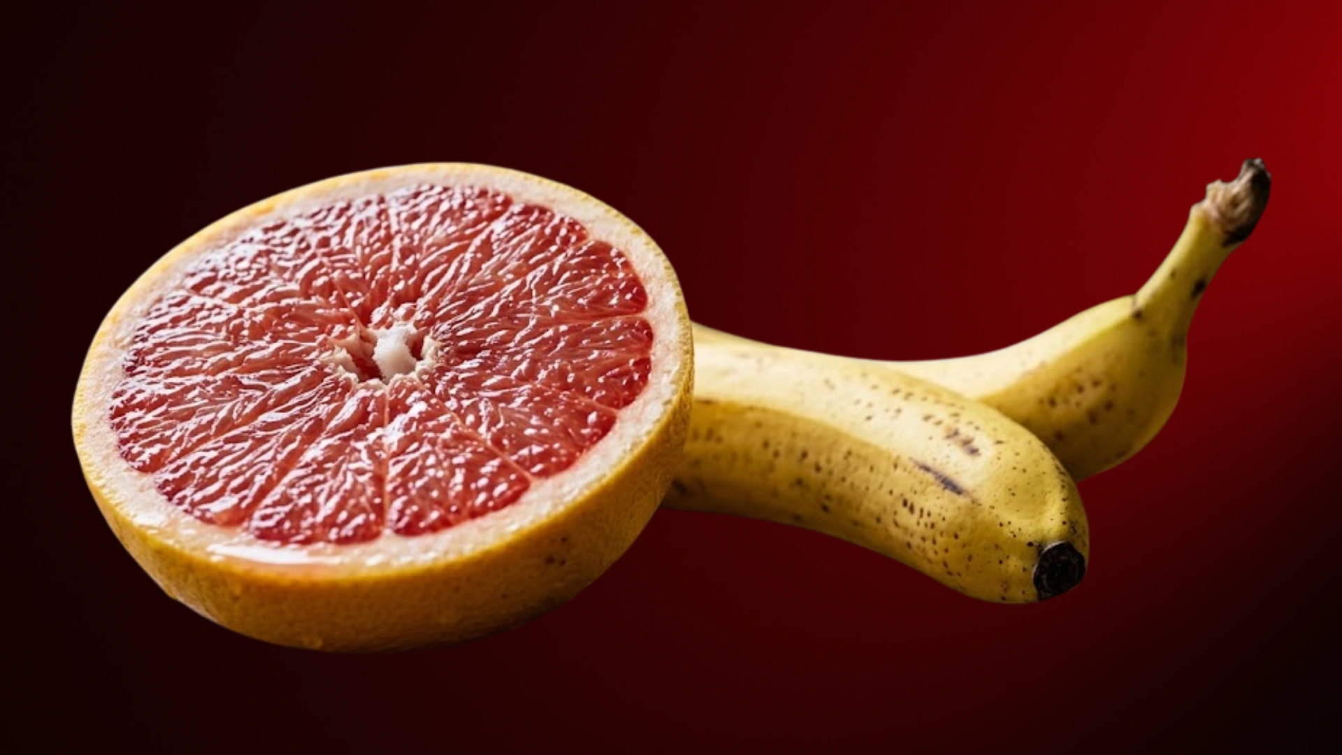 Half a grapefruit next to two bananas on a red background.
