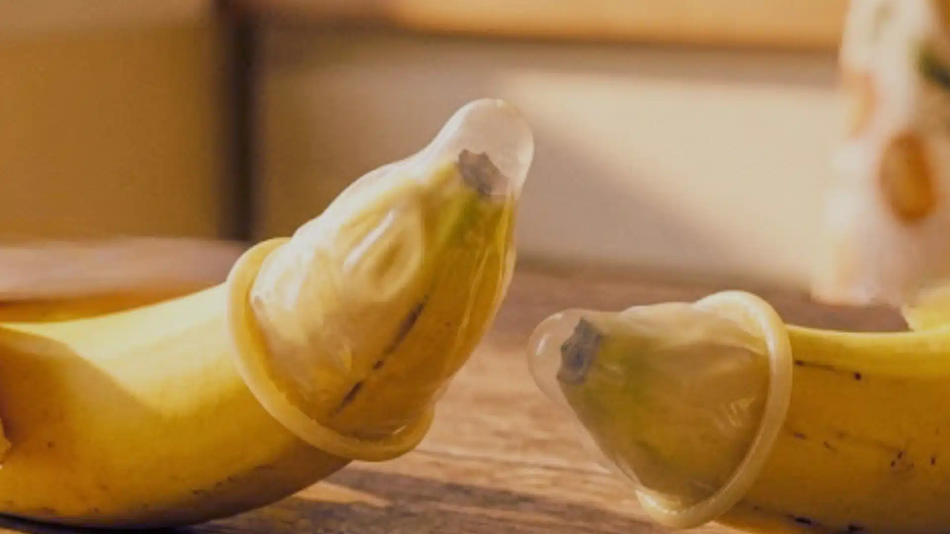 Two bananas lying on a table, each covered with a condom, one larger than the other.
