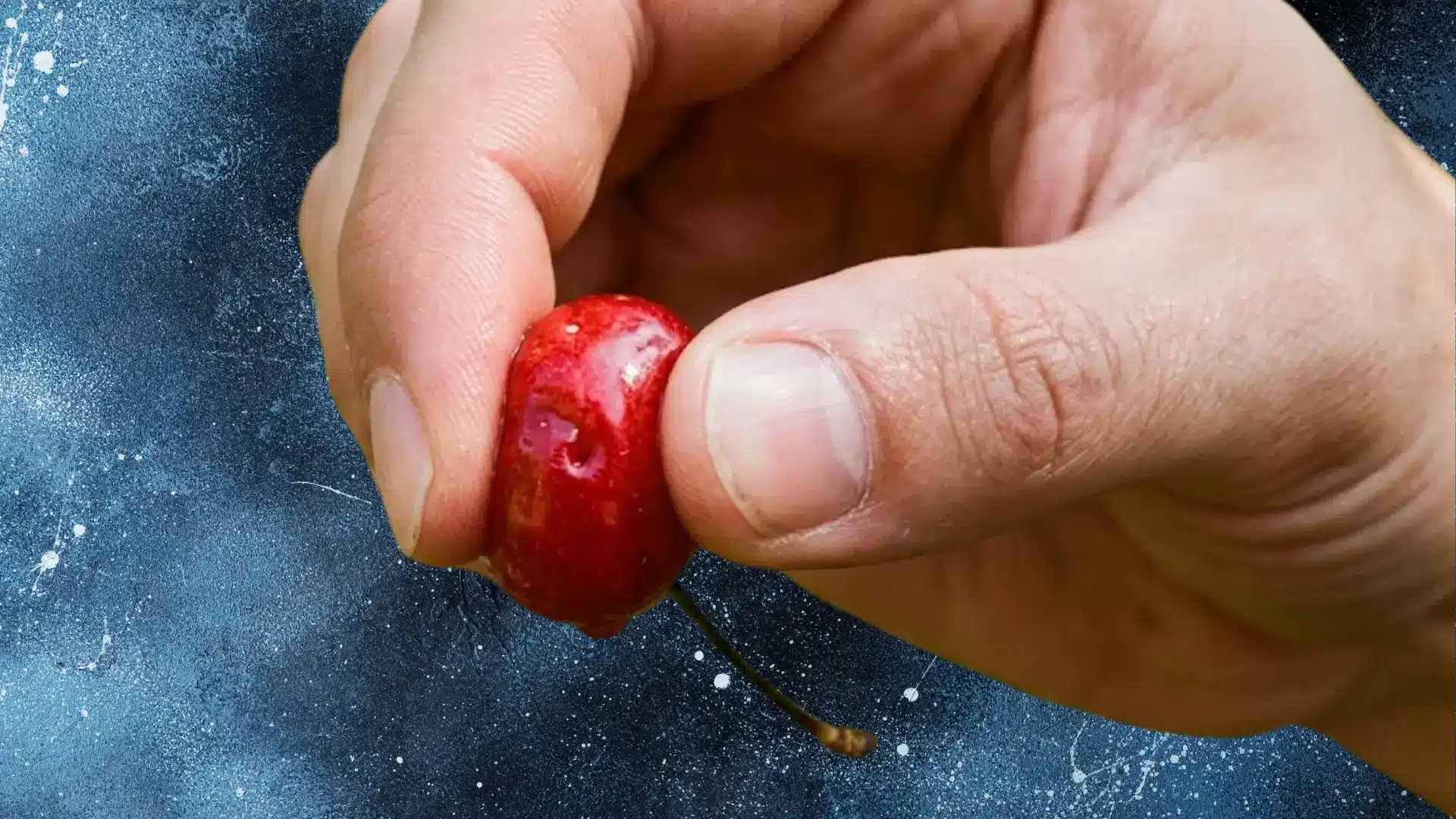 Hand squeezing a bright red cherry between fingers, symbolizing gentle nipple massage, sensitivity, pressure, and intimate touch.