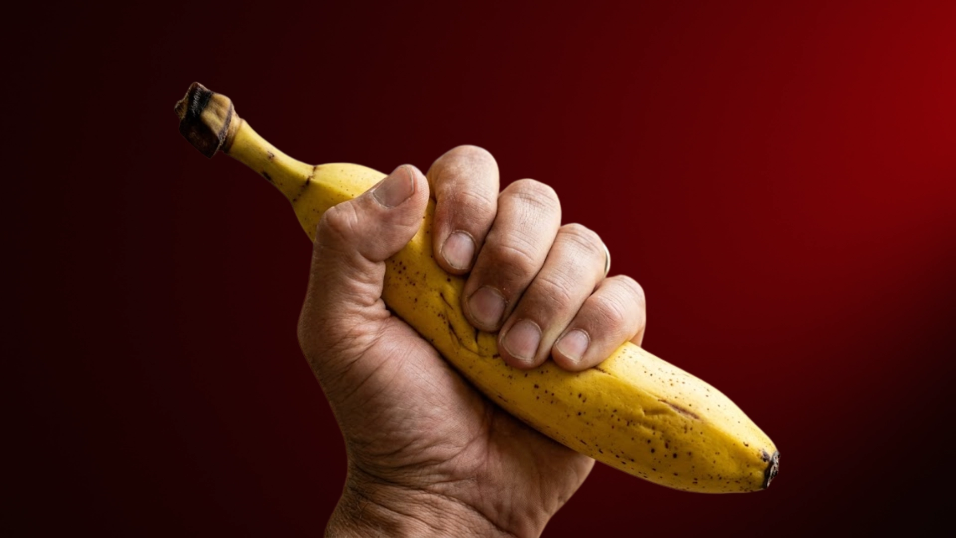 A hand holding a banana against a red background