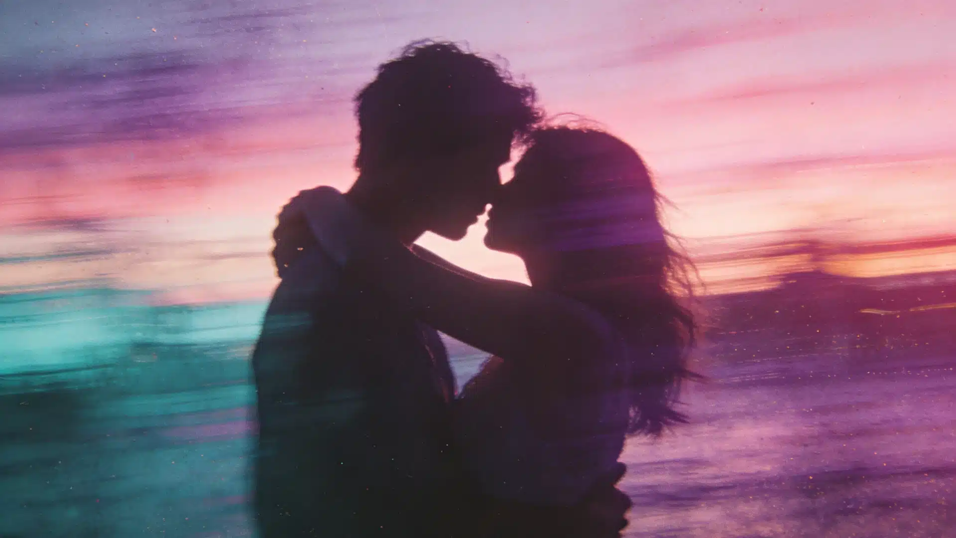 A couple shares a kiss against a vibrant sunset, with warm colors illuminating their silhouettes