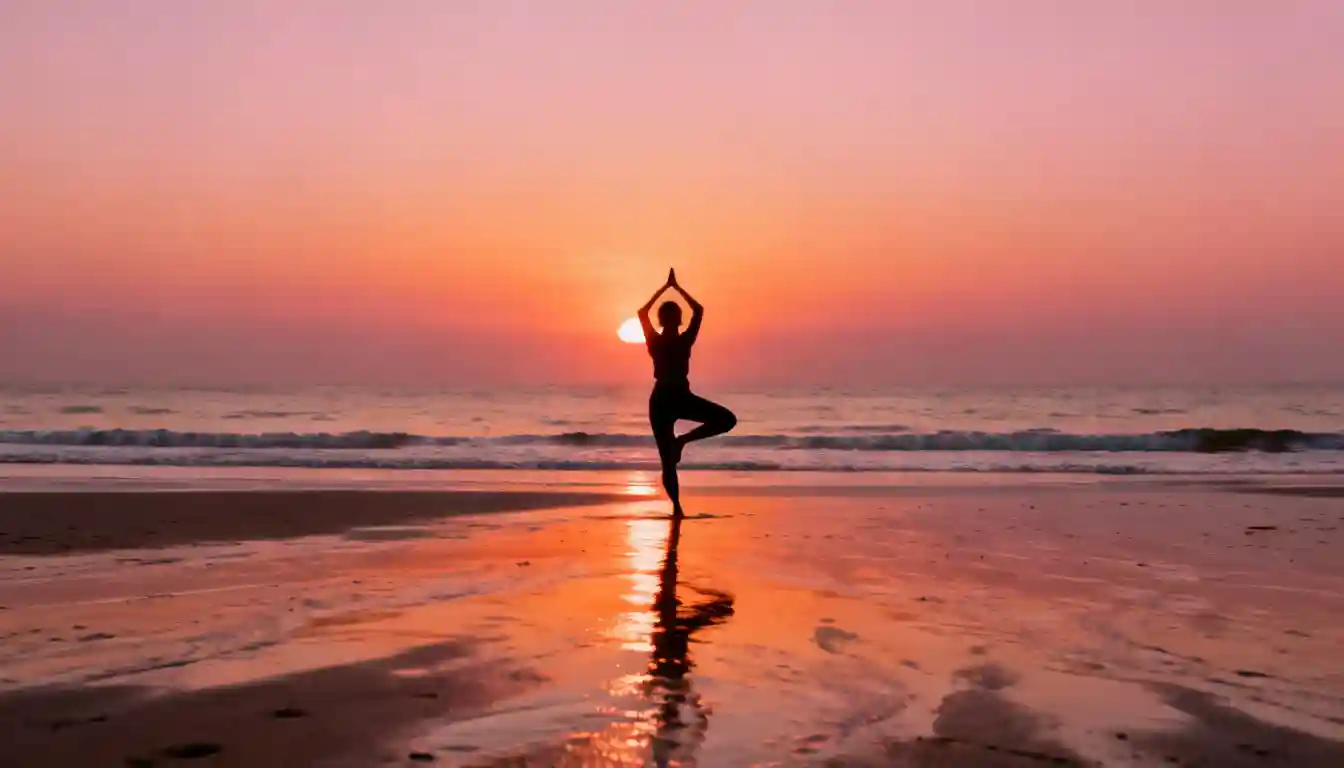 Silhouette of a person practicing yoga's Tree Pose on a wet beach at sunset.