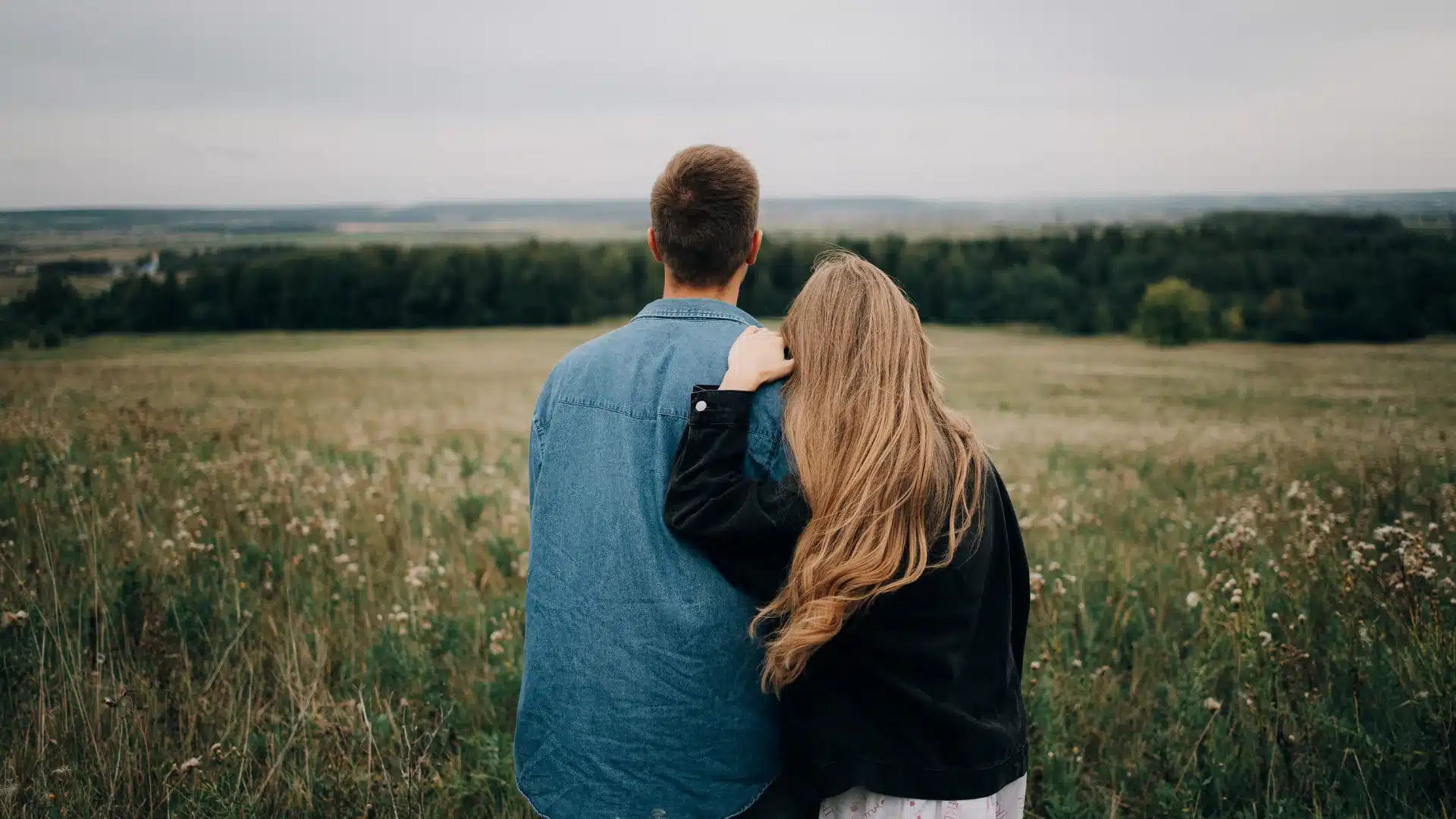 A man and woman stand together in a lush green field, smiling and enjoying the outdoors